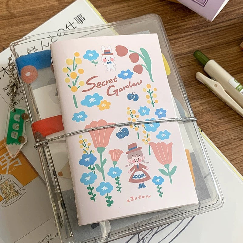 Notebook with floral design and 'Secret Garden' text, placed in a clear plastic case on a wooden surface.